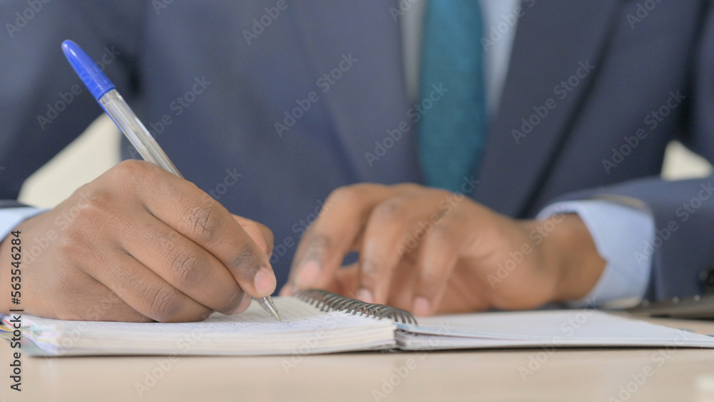 Close Up of Young African Businessman Hand Writing on Notebook Close Up of Young African Businessman Hand Writing on Notebook