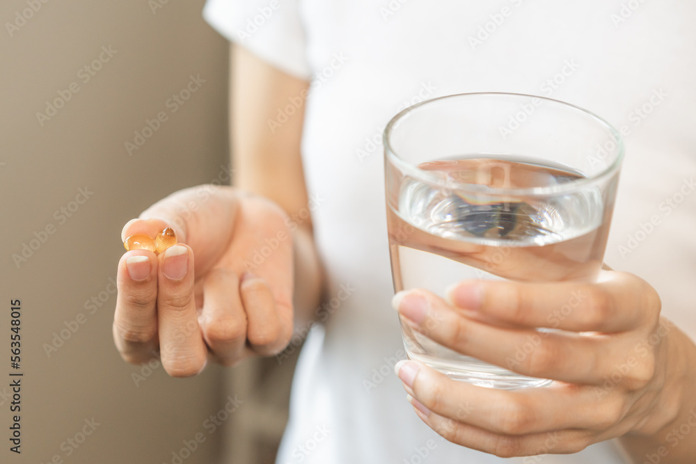 Dietary supplement, asian young woman hand holding fish oil or medical pill, take or eat vitamin C, D for treatment for skin, hair and nail strengthen with glass of pure water at home, healthcare. Dietary supplement, asian young woman hand holding fish oil or medical pill, take or eat vitamin C, D for treatment for skin, hair and nail strengthen with glass of pure water at home, healthcare.