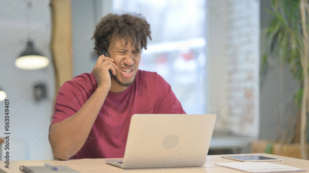 Displeased African Man Talking Angrily on Smartphone at Work Displeased African Man Talking Angrily on Smartphone at Work