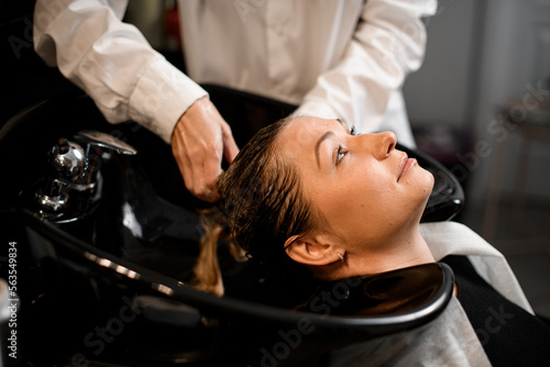 Close-up of female client relaxed on hair washing chair while hairdresser washes her hair