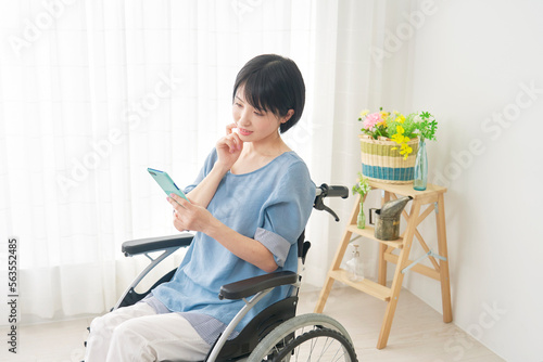 家でスマホを使う車椅子に乗った障がい者女性
