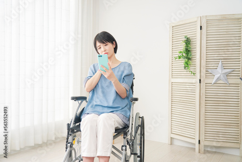 家でスマホを持って考える車椅子に乗った障がい者女性 コピースペースあり