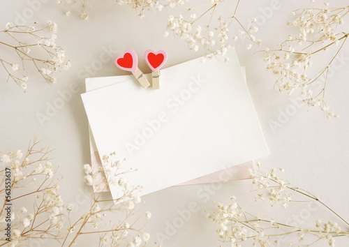 Valentines Day blank papers, greeting cards mockup with clothespins hearts and flowers top view on beige background.