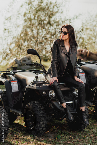 sexy girl with long dark hair on quad bike; dressed in black leather clothes; sunglasses on the eyes; posing on a quad bike