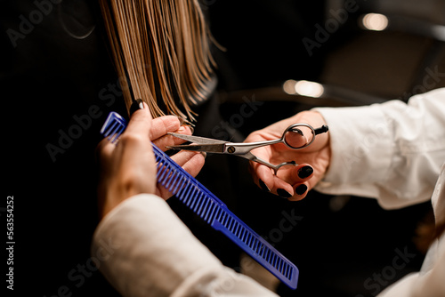 Hands of hairdresser with comb and scissors in process of accurate haircut health female hair in salon.