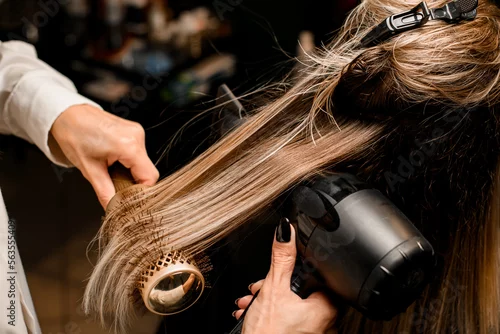 Obraz Close-up of hairdo making process. Hairdresser puts female hair with dryer and comb