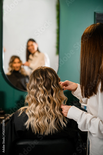 great rear view of woman with perfect curl hair and hairdresser in hair salon