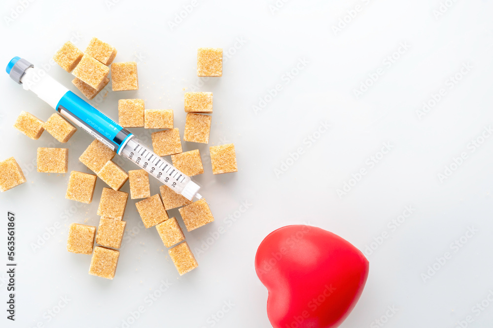 Human insulin pen on top of brown sugar cane cubes with red heart symbol on white reflective glass.  Diabetes concept. Healthy concept.