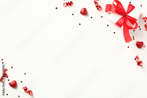 Fat lay composition with gift box adorned with a red ribbon bow, confetti, and heart-shaped candies on a white background. Valentine's Day, love, romance concept.