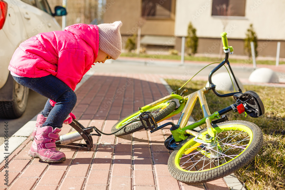 Naklejka premium a little girl pumps up a bicycle tire.