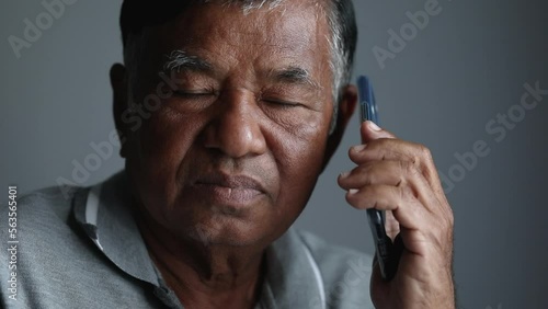 Asian elderly man serious while talking on the phone. Sad old man alone using a smartphone at home photo