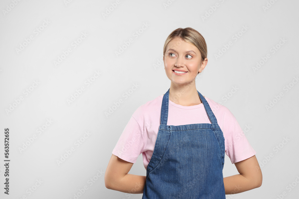 Beautiful young woman in denim apron on light grey background. Space for text Beautiful young woman in denim apron on light grey background. Space for text