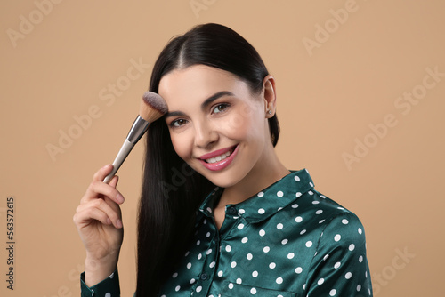 Beautiful woman applying makeup on light brown background