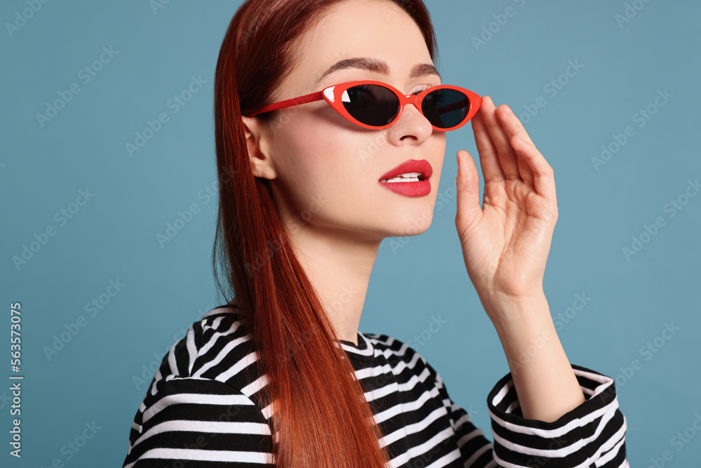Stylish woman with red dyed hair and sunglasses on light blue background Stylish woman with red dyed hair and sunglasses on light blue background