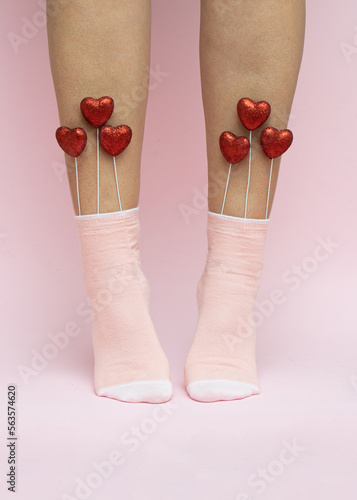 Red hearts in pink women's socks. Valentine's Day love concept on pink background. Minimal romantic idea.
