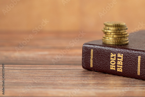 Stack of golden coins on top of holy bible book on a wooden background. Copy space for text. A closeup. Christian tithing, giving, and religious offering concept. photo