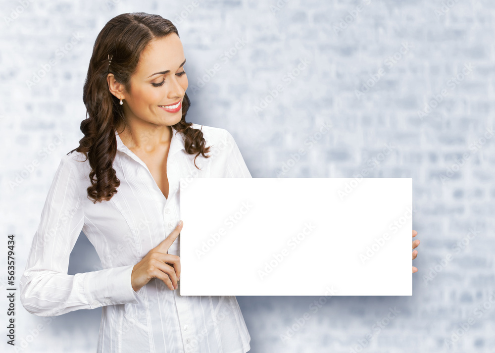 Cheerful smiling brunette business woman in white confident clothing showing empty mock up signboard. Success and advertising concept. Copy space place, white bricks wall background. Cheerful smiling brunette business woman in white confident clothing showing empty mock up signboard. Success and advertising concept. Copy space place, white bricks wall background.