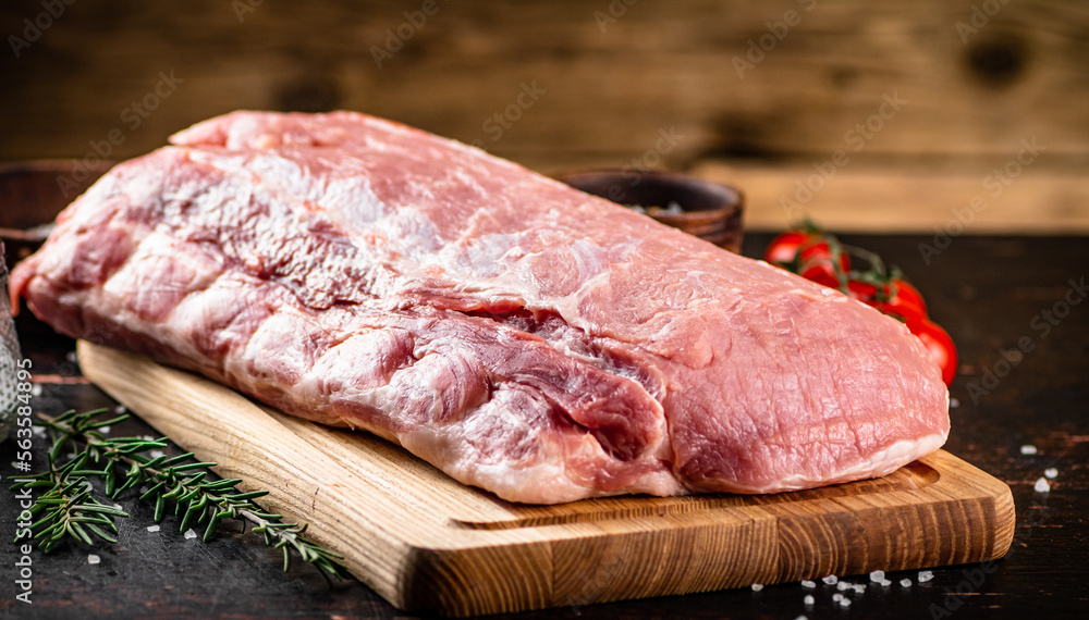 Raw pork on a cutting board with fresh tomatoes. 