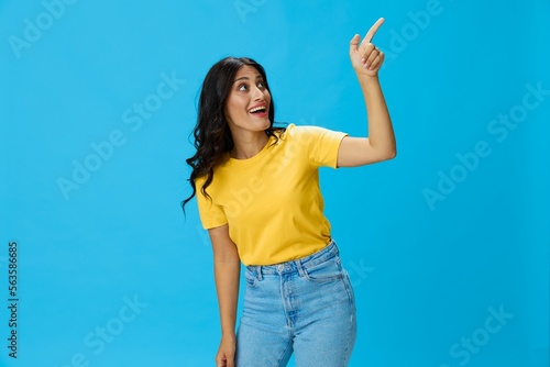 Woman in yellow t-shirt on blue background posing gestures emotions and signals with smile, hands up happiness copy space