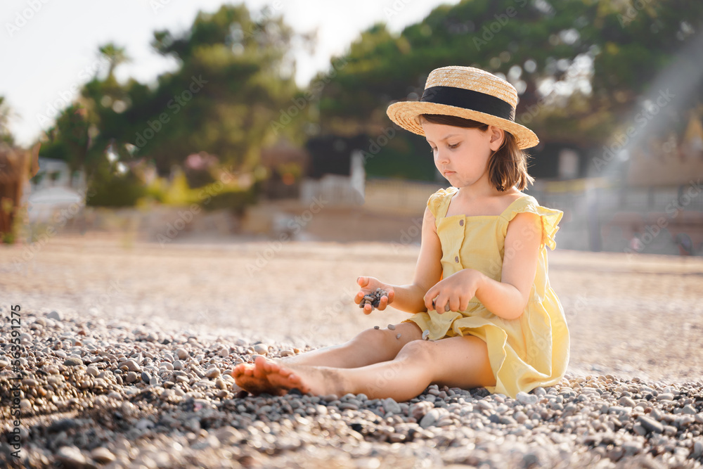 Little girl walking on beach, sea ocean shore in romantic yellow dress, straw hat. Playing in sand, blue waves. Family vacation travel leisure in hot summer coast. Sunny day relax in hotel resort