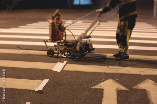 Process of making new road surface markings with line striping machine, workers improve city infrastructure, demarcation marking of pedestrian crossing with hot melted paint on asphalt pavement