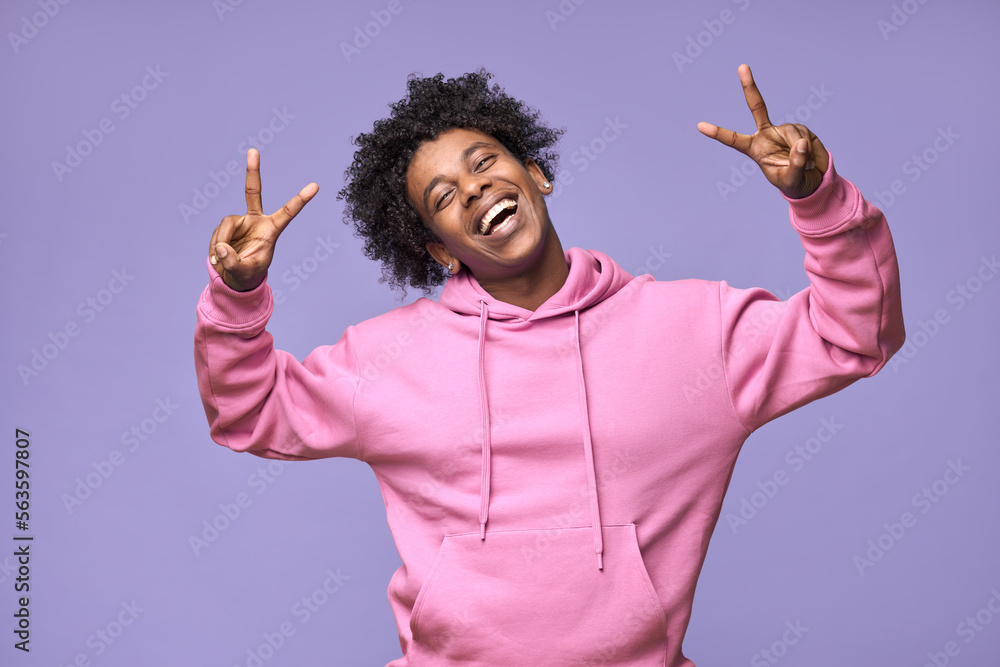 Young cheerful happy hipster African American teen guy wearing pink hoodie isolated on light purple background. Smiling cool joyful ethnic generation z teenager model laughing showing peace sign. - obrazy, fototapety, plakaty 