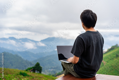 Young man freelancer traveler working online using laptop and enjoying the beautiful nature landscape with mountain view