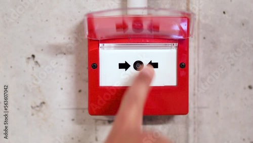 Close up of male hand pointing at red fire alarm switch on concrete wall in office building. Industrial fire warning system equipment for emergency at factory