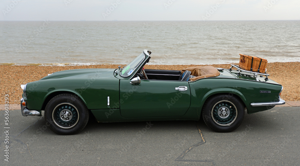 Classic Green Spitfire Mk 4  motor  car with picnic basket on boot parked on Seafront Promenade beach and sea in background. 