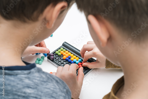 Top view of two boys friends playing colorful 3D puzzle classic pyramid game, putting beads in order on black board.