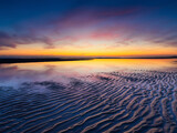 A seascape during sunset. Lines of sand on the seashore. Bright sky during sunset. A sandy beach at low tide. Travel image.