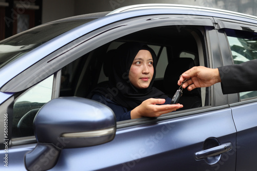 Salesman gives car keys to muslim woman client after successful retail deal in dealership centre.