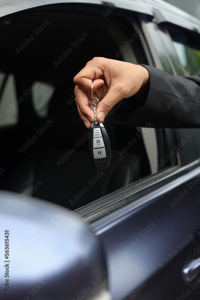 Cropped image of car salesman handing over your new car keys at car window, dealership and sales concept.