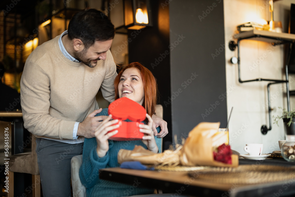 Valentines day couple sitting in favourite caffe, exchanging gifts in hart shape