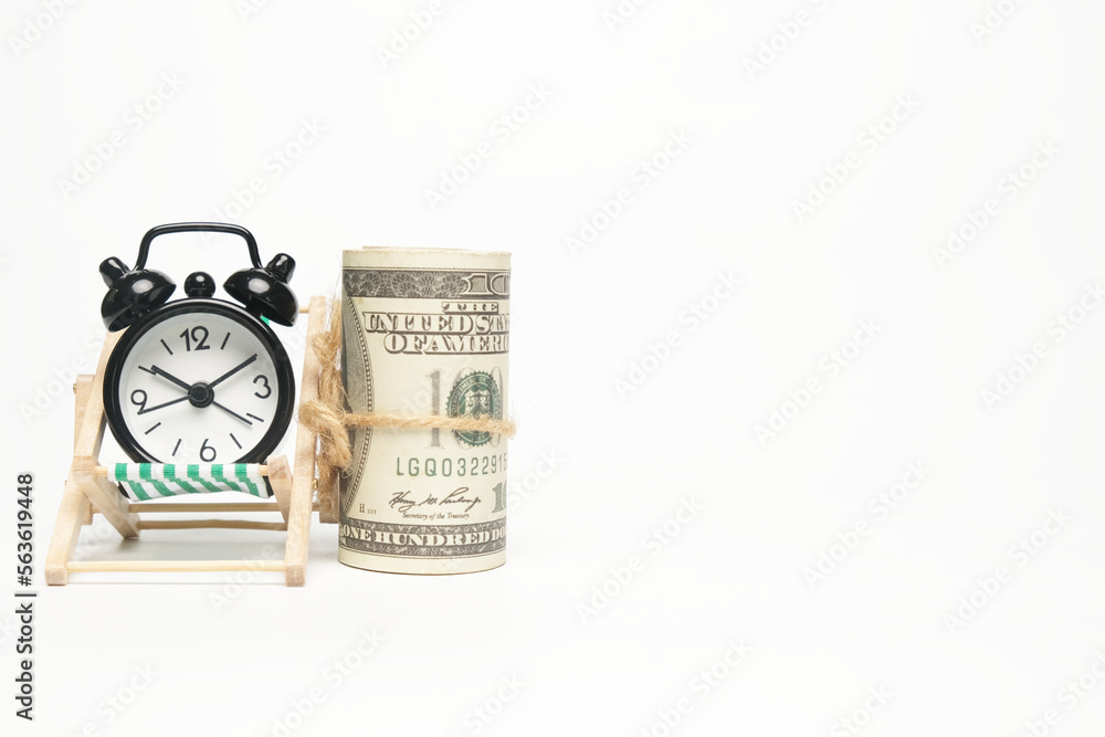 Selective focus picture roll fake money on folding beach chair and alarm clock on copyspace white background . Future financial and work life balance concept. Selective focus picture roll fake money on folding beach chair and alarm clock on copyspace white background . Future financial and work life balance concept.
