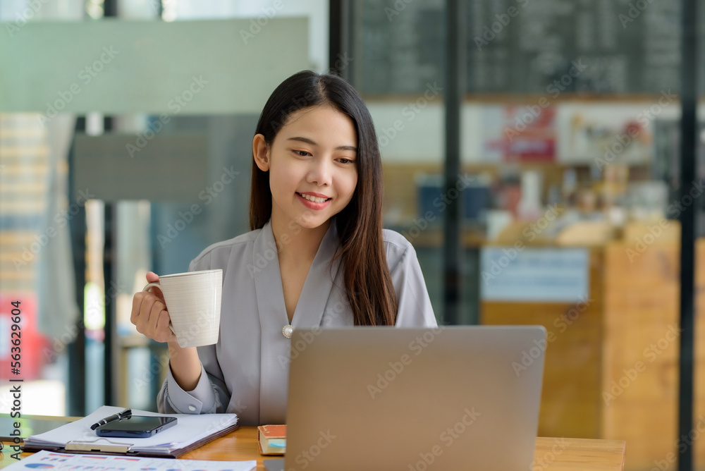 Beautiful asian businesswoman sitting and working in cafe smiling and enjoying work while having coffee and working happily with laptop computer. Beautiful asian businesswoman sitting and working in cafe smiling and enjoying work while having coffee and working happily with laptop computer.