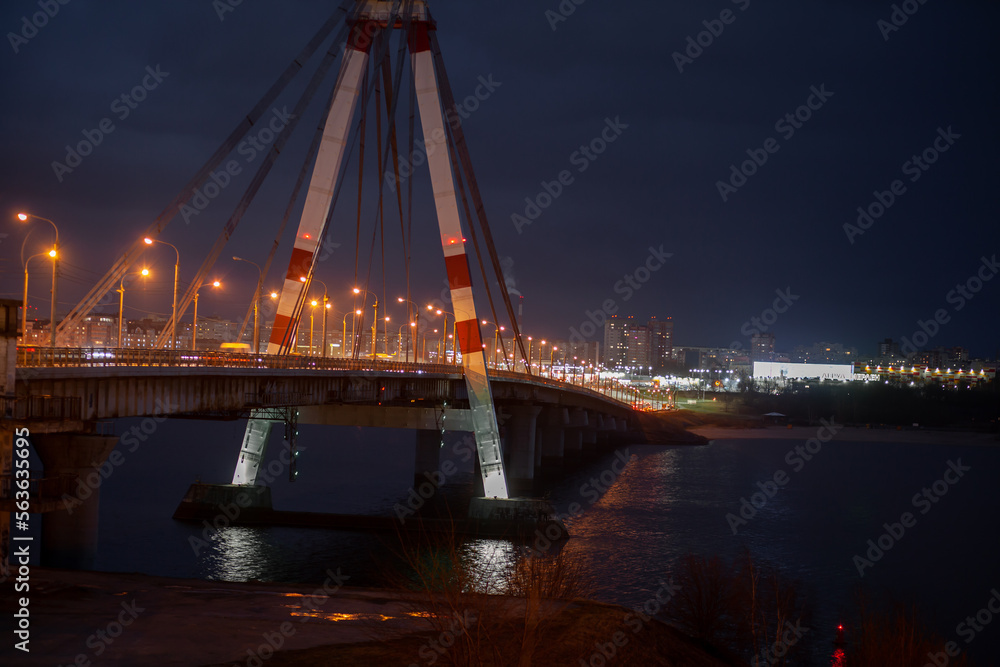 A large automobile bridge on which cars drive at night. A bridge with large columns and lighting.