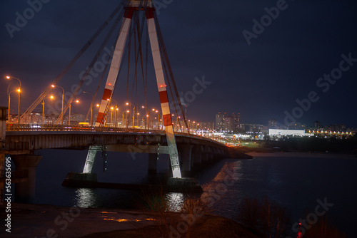 A large automobile bridge on which cars drive at night. A bridge with large columns and lighting.
