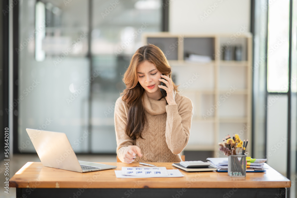 Businesswoman using the phone to talk to customers In the office there is a laptop on the desk.. Businesswoman using the phone to talk to customers In the office there is a laptop on the desk..