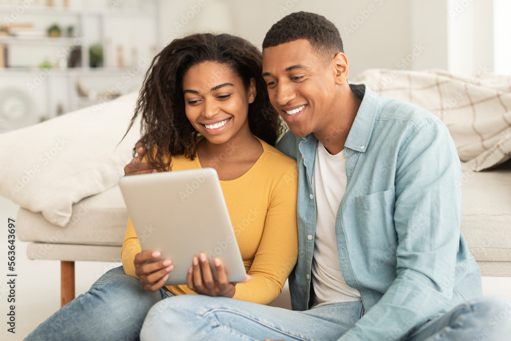 Technology for new normal at home. Glad millennial african american man and lady hug looking at digital tablet Technology for new normal at home. Glad millennial african american man and lady hug looking at digital tablet