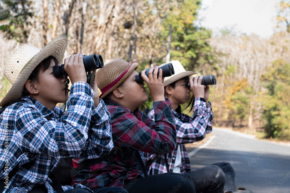 Obraz premium Asian boys are using binoculars to do the birds' watching in tropical forest during summer camp, idea for learning creatures and wildlife animals and insects outside the classroom.