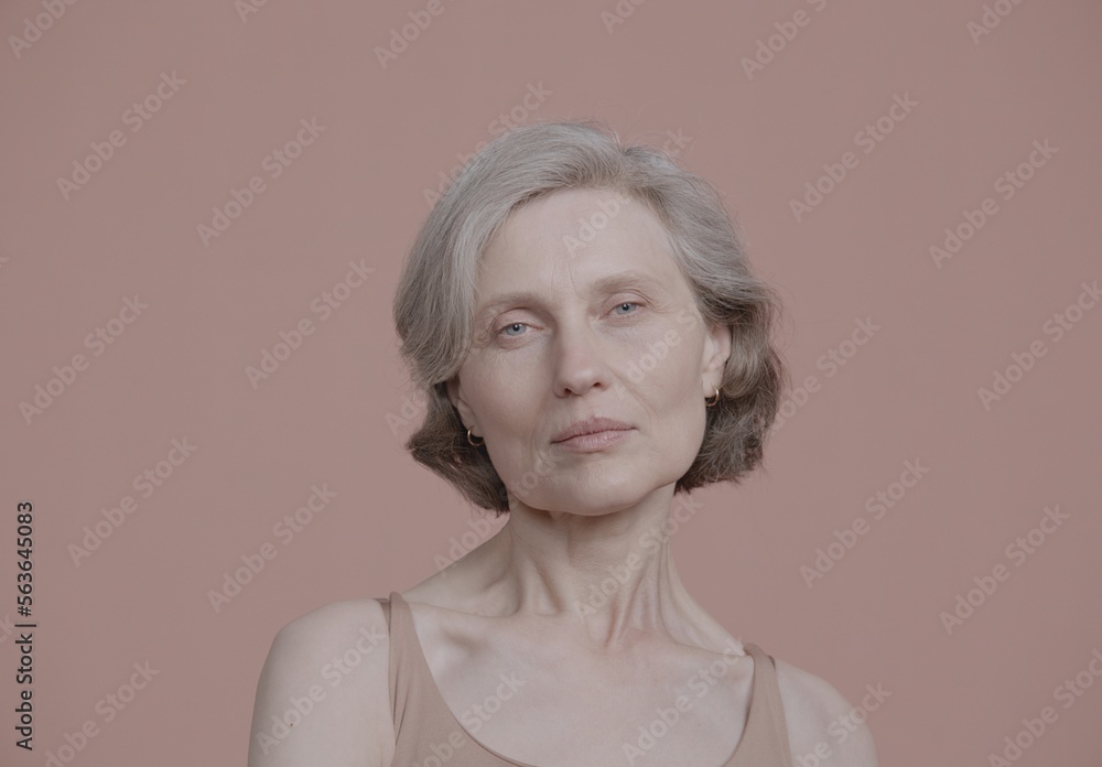CU Portrait of beautiful 60s mature senior adult female posing without makeup against light brown background. Studio shot, soft lighting. No make up, clean skin CU Portrait of beautiful 60s mature senior adult female posing without makeup against light brown background. Studio shot, soft lighting. No make up, clean skin