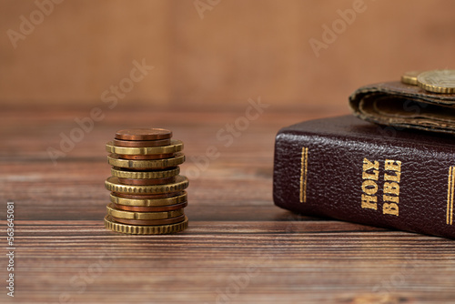 Photography Stack of coin money, holy bible book and old wallet on wooden table