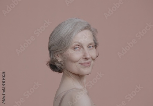 CU Portrait of beautiful 60s grey-haired mature senior adult female posing without makeup against light brown background. Studio shot, soft lighting. No make up, clean skin
