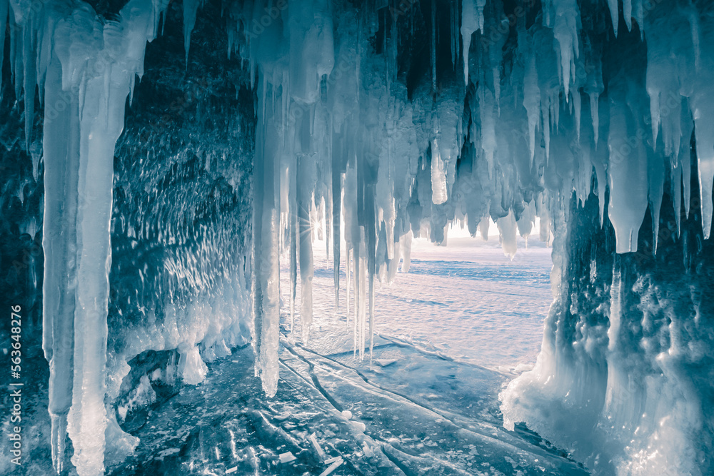 Ice cave with icicles on Baikal lake at sunset.