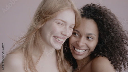 Candid portrait of two beautiful 20s females, African-American Black and Caucasian, posing against solid background, no make-up, studio shot, soft lighting
