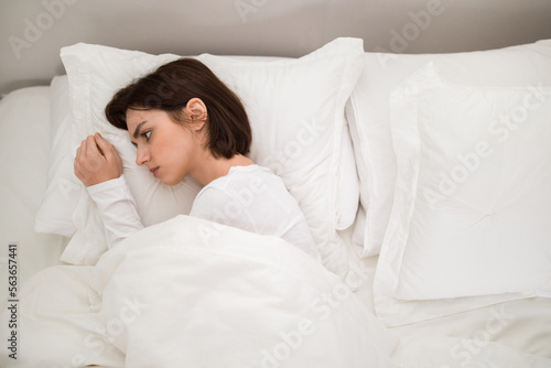 Upset young woman lying alone in bed, top view