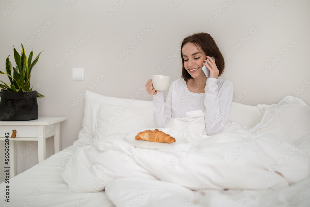 Cheerful young woman have breakfast in bed, talking on phone Cheerful young woman have breakfast in bed, talking on phone