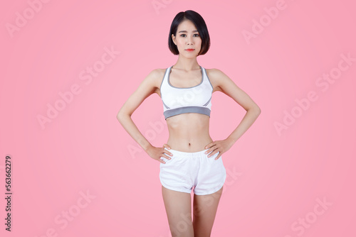 Confident sportswoman in white sportsbra, holding hands on waist, fitness trainer standing in power pose, workout in gym, pink background.