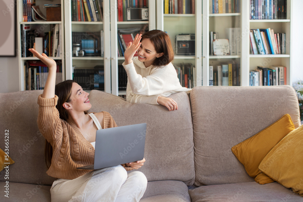 Cheerful european young women with laptop give high five gesture, surfing internet, have fun enjoy win